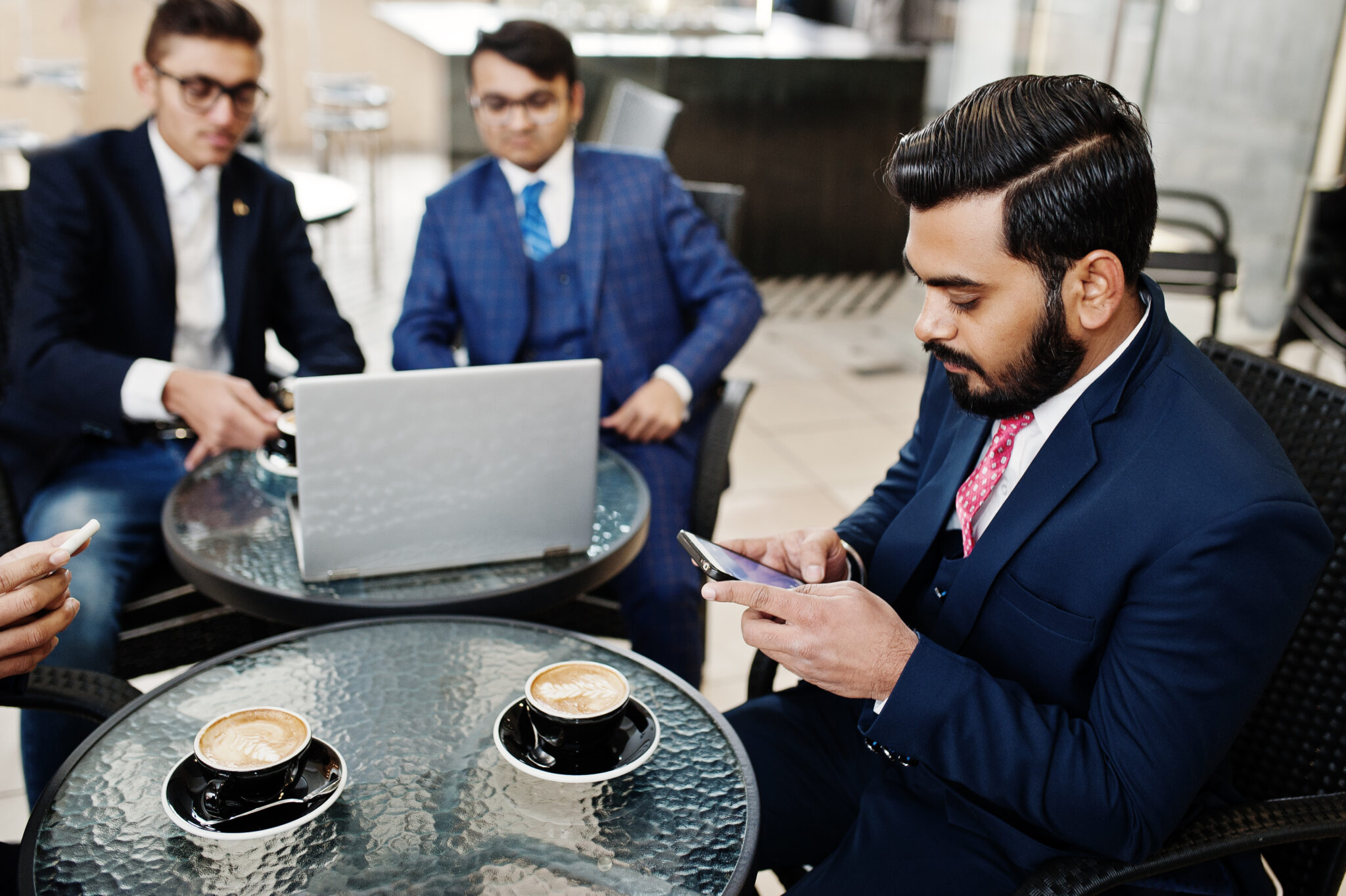 Group of indian business man in suits sitting at office on cafe with laptop, texting on phones and making photo of coffee.