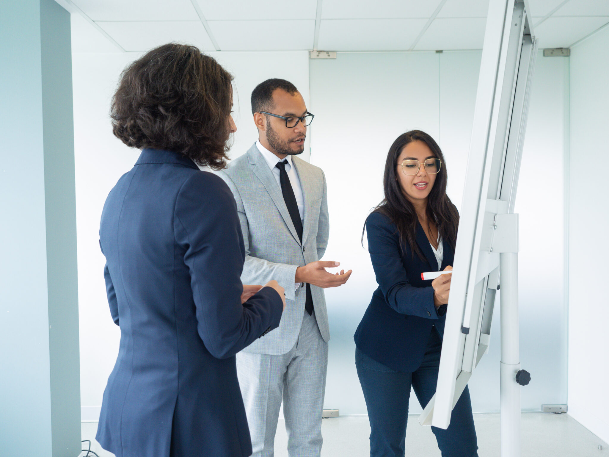 Manager presenting company strategy to customers. Business woman drawing on board, her two colleagues looking at drawing. Presenting strategy concept